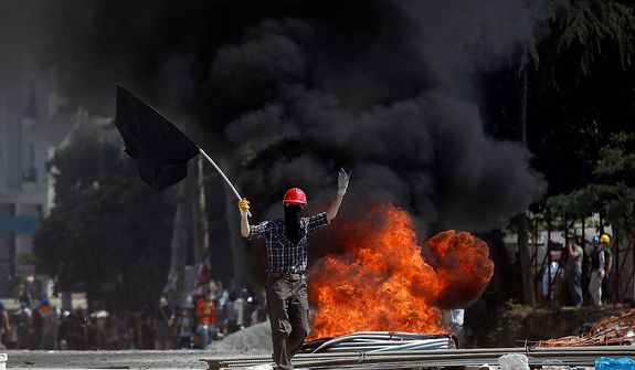 A protester gestures to riot police as he walks in front of a burning barricade during clashes in Taksim Square in Istanbul on Tuesday, June 11, 2013. Hundreds of police in riot gear forced through barricades and pushed many of the protesters who had occupied the square for more than a week into a nearby park. (AP Photo/Kostas Tsironis)