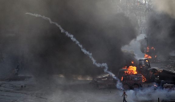 A protester throws tear gas at police as a bulldozer blazes during clashes in Taksim Square in Istanbul on Tuesday, June 11, 2013. Hundreds of riot police overran improvised barricades on the central square and fired tear gas, rubber bullets and water cannon in running battles with protesters who have been occupying the area for more than a week. (AP Photo/Thanassis Stavrakis)