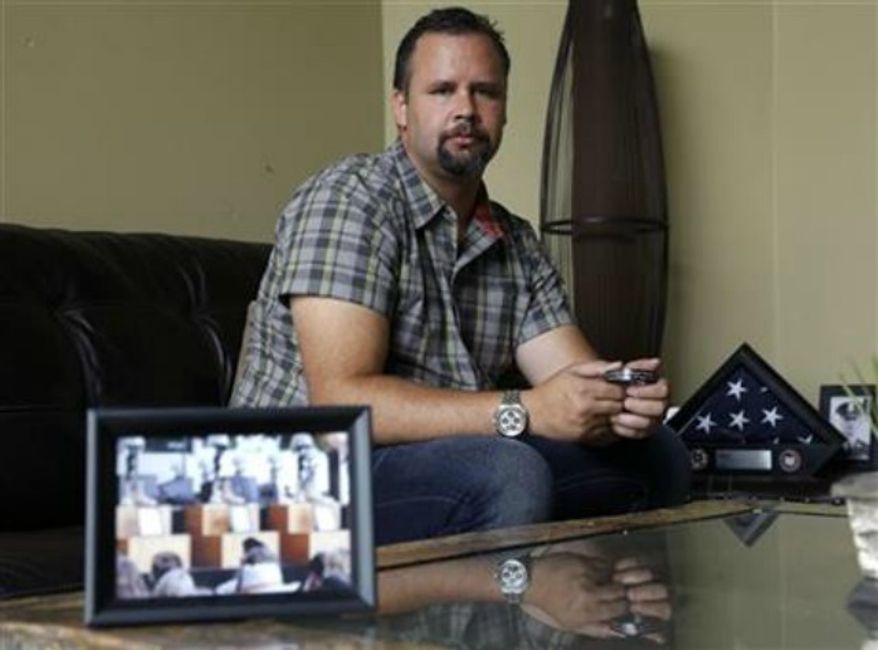 ** FILE ** Retired U.S. Army Staff Sgt. Shawn Manning poses for a photo at his home in Lacey, Wash., as he holds a photograph from the memorial for victims of the 2009 mass shooting at Fort Hood, Texas, Aug. 3,, 2013. Manning, who still carries two bullets in his body from the shooting that killed 13 people, estimates he has lost $2,000 a month in pay and benefits because of the decision to classify the injuries as resulting from workplace violence rather than combat or terrorist-related. (AP Photo/Ted S. Warren, File)