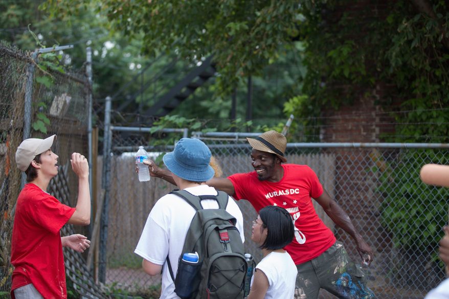 Aniekan Udofia laughs with his apprentices during a break from priming the wall for his mural on Florida Avenue Northwest that is part of a graffiti-prevention program. (Andrew S. Geraci/The Washington Times)