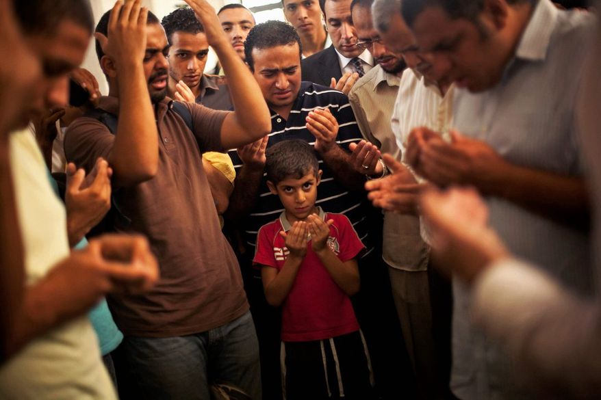 Mass Mourning: A son of Ammar Badie prays during his father's funeral Sunday. Mr. Badie, a son of the Muslim Brotherhood's spiritual leader Mohammed Badie, was killed by Egyptian security forces Friday during clashes in Cairo. (Associated Press)
