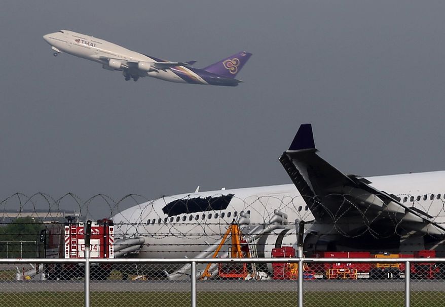 A Thai Airways passenger plane takes off over a damaged Thai Airways Airbus A330-300 at Suvarnabhumi International Airport in Bangkok, Thailand Monday, Sept. 9, 2013. (AP Photo/Apichart Weerawong)