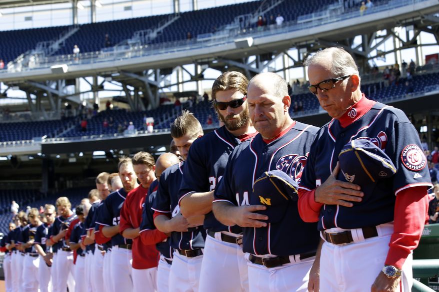 Holding Navy hats, Washington Nationals manager Davey Johnson, right, and others observe a moment of silence before a baseball game against the Atlanta Braves at Nationals Park Tuesday, Sept. 17, 2013, in Washington. The Nationals wore Navy hats, presented to them by Adm. James A. Winnefield, vice-chairman of the Joint Chiefs of Staff, before the game, to honor those killed and injured in the attack Monday at the nearby Washington Navy Yard. (AP Photo/Alex Brandon)