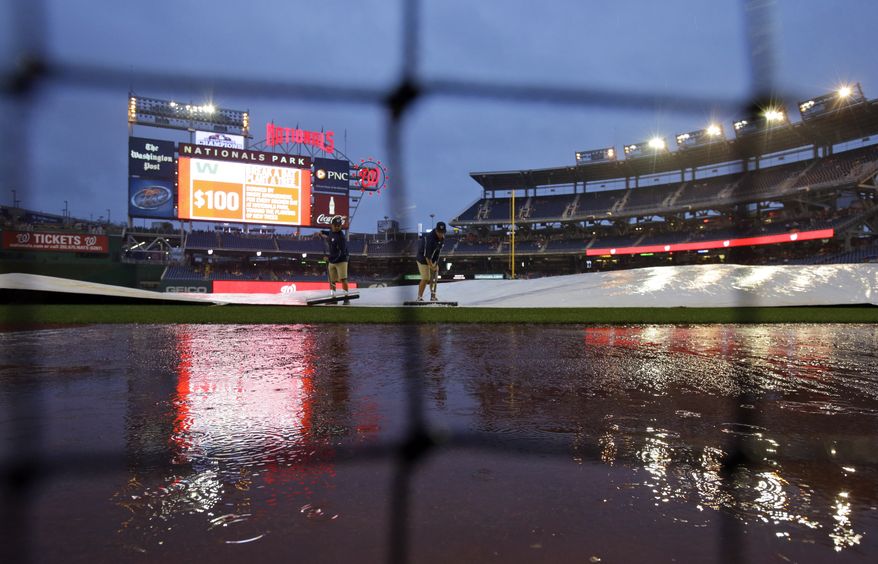 The Washington Nationals' grounds crew squeegees water off the tarp during a three-hour, 49-minute rain delay on Saturday night. The game was postponed until Sunday night. (Associated Press photo)