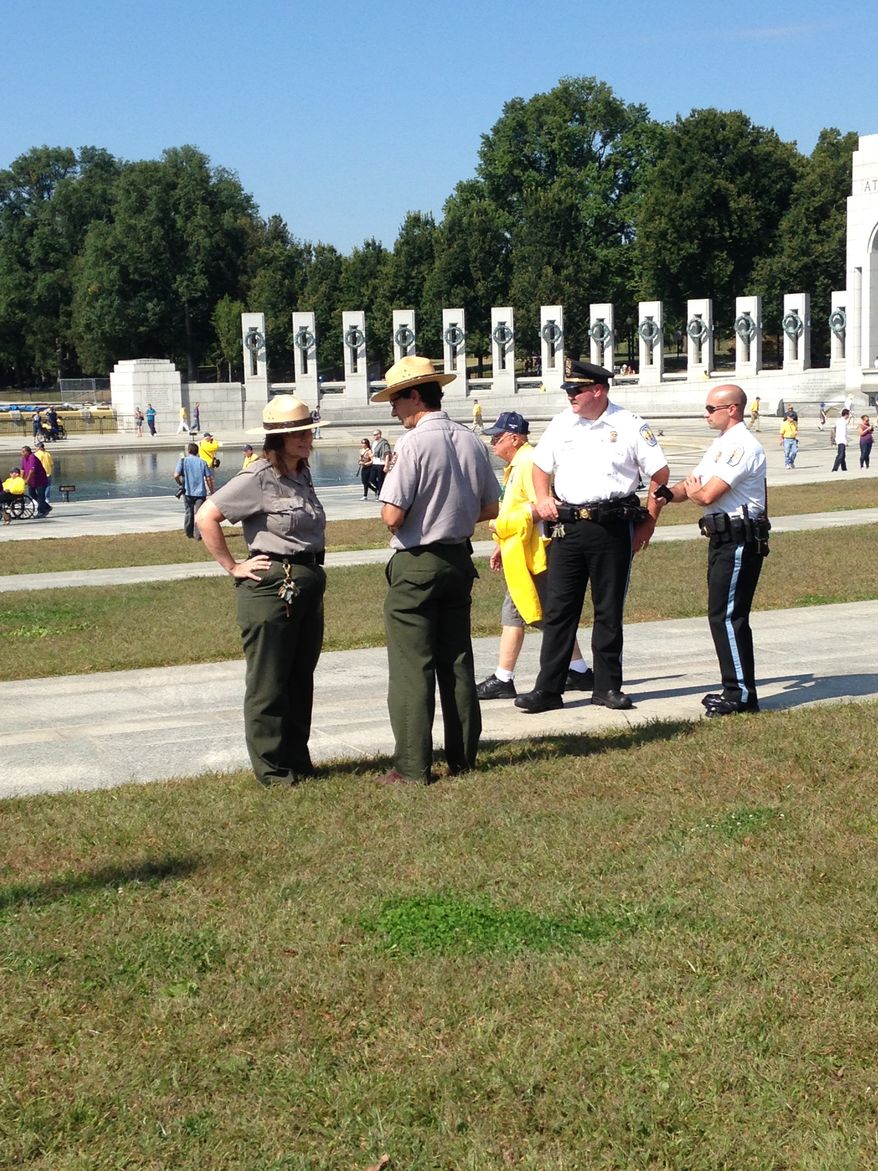 U.S. Park Police and National Park Service personnel watch after a group that included elderly veterans forced their way into the World War II Memorial closed because of the government shutdown. (David Sherfinski/The Washington Times)