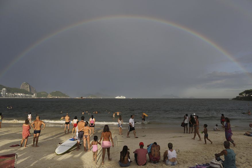 In this Tuesday, Dec. 31, 2013 photo, a rainbow arches across the horizon during New Year's Eve festivities on Copacabana beach in Rio de Janeiro, Brazil. Sugar Loaf is pictured on left. (AP Photo/Leo Correa)