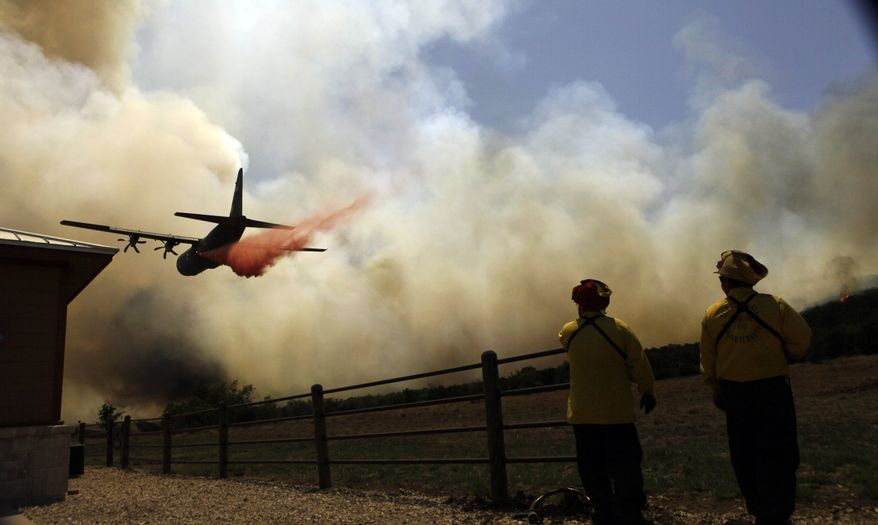 **FILE** Firefighters look on as an air tanker makes a pass over a wildfire near Possum Kingdom, Texas, on April 19, 2011. (Associated Press)