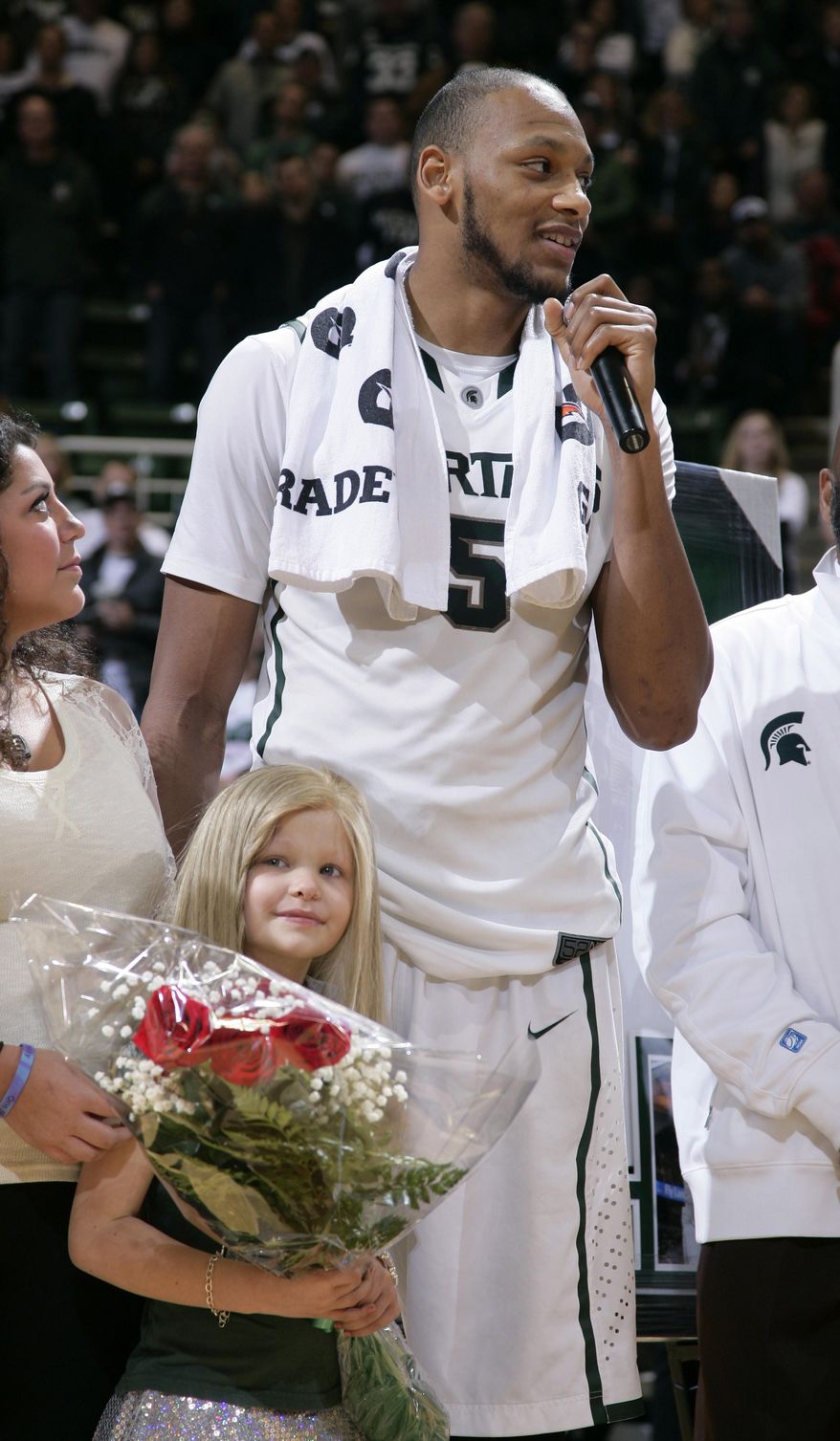 ** FILE ** In this March 6, 2014, file photo, Michigan State senior Adreian Payne addresses the crowd during a senior day ceremony as he stands with his guest, Lacey Holsworth, who is battling cancer, following an NCAA college basketball game against Iowa, in East Lansing, Mich. The father of 8-year-old Lacey Holsworth, who befriended Michigan State basketball star Adreian Payne says his daughter has died. (AP Photo/Al Goldis)