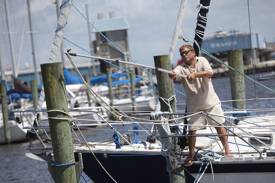 Oriental Harbor Marina dock master Mark Crowden stretches to loop an extra dock line around a post Wednesday afternoon, July 2, 2014, in Oriental, N.C. Although it's the boat owner's responsibility, he will walk the marina making sure the boats are safe and have enough dock lines to keep the boat and dock from crashing into each other during large waves expected from Tropical Storm Arthur as it brushes by Oriental. (AP Photo/Sun Journal, Chuck Beckley)
