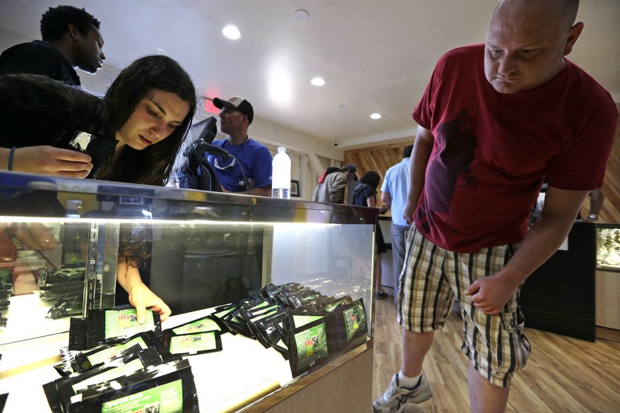 Clerk Havilah Nokes arranges packets of marijuana for sale as a customer peers in at the display at Cannabis City on the first day of legal recreational pot sales Tuesday, July 8, 2014, in Seattle. Washington on Tuesday became the second state to allow people to buy marijuana legally in the U.S. without a doctor's note as eager customers who lined up outside stores made their purchases. (AP Photo/Elaine Thompson)
