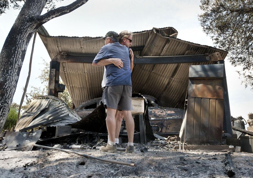 Bill Cleek, left, embraces his good friend, Terry Cromwell outside a structure which housed one of many antique cars destroyed by a fire at Rancho Cicada Retreat on Sunday, July 27, 2014, in Plymouth, Calif. Firefighters in Northern California on Sunday battled a wildfire that has destroyed 10 homes and forced hundreds of evacuations in the Sierra Nevada foothills, while a fire near Yosemite National Park destroyed one home and grew significantly overnight. (AP Photo/The Sacramento Bee, Randy Pench)