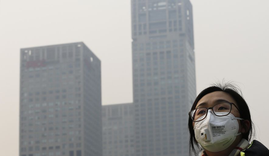 A woman wearing a face mask to protect herself from pollutants walks past office buildings shrouded with pollution haze in Beijing, Monday, Dec. 7, 2015. Beijing issued its first-ever red alert for smog on Monday, urging schools to close and invoking restrictions on factories and traffic that will keep half of the city&#39;s vehicles off the roads. (AP Photo/Andy Wong)