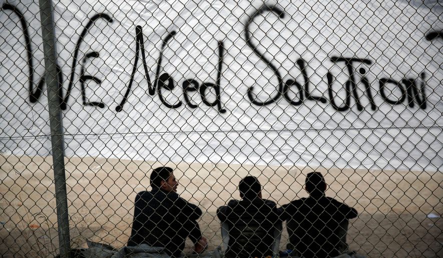 Migrants sit below a banner outside a former Olympic indoor stadium in Faliro, southern Athens        Associated Press photo
