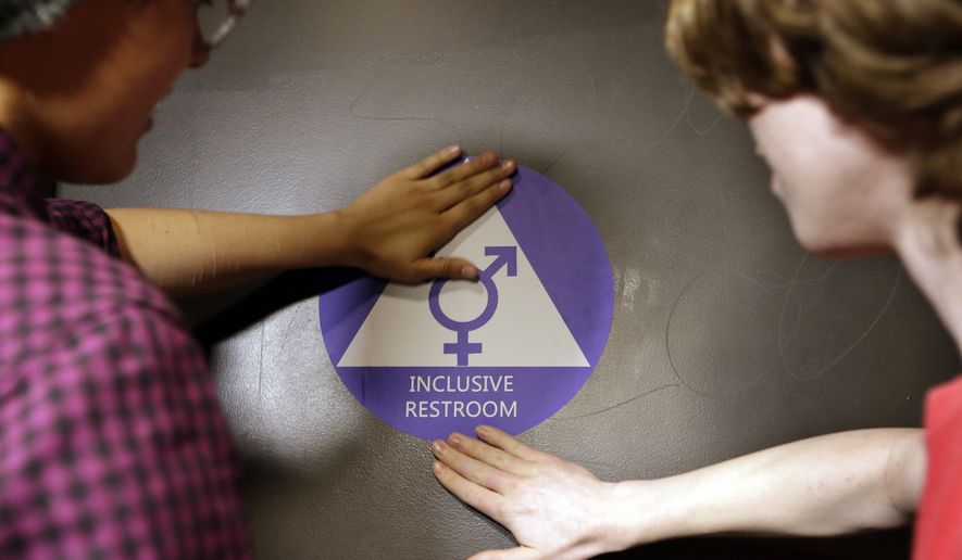 Destin Cramer, left, and Noah Rice place a new sticker on the door at the ceremonial opening of a gender neutral bathroom at Nathan Hale high school May 17 in Seattle. (Associated Press)
