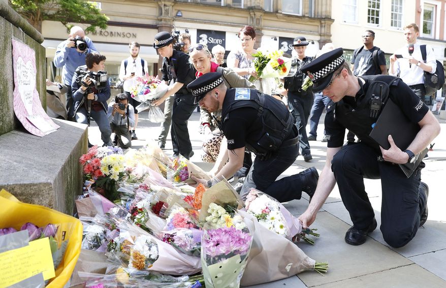 Police offices add to the flowers for the victims of Monday night pop concert explosion, in St Ann's Square, Manchester,  Tuesday May 23, 2017. A 23-year-old man was arrested in connection with Monday's Manchester concert bomb attack. The Islamic State group claimed responsibility Tuesday for the suicide attack at an Ariana Grande show that left over 20 people dead and dozens injured. ( Martin Rickett/PA via AP)