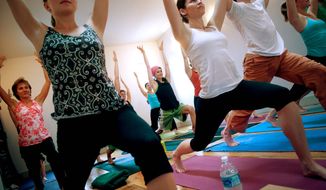 ALLISON SHELLEY/THE WASHINGTON TIMES
Amanda Galzer (front row, left), Lauren Weeman (white tank top) and others move into the Warrior I pose during a Yoga III class at Tranquil Space Yoga.