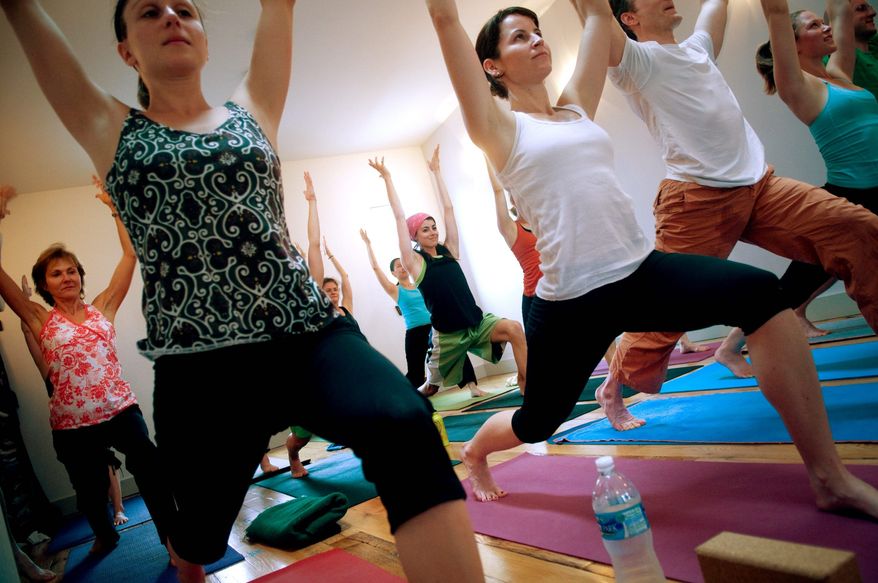 ALLISON SHELLEY/THE WASHINGTON TIMES
Amanda Galzer (front row, left), Lauren Weeman (white tank top) and others move into the Warrior I pose during a Yoga III class at Tranquil Space Yoga.