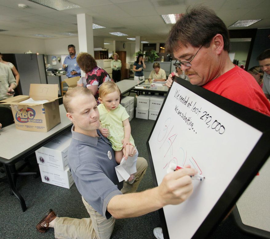 Tim Eyman holds his daughter Riley, 1, in July 2009 while updating a board tallying petition signatures for getting an initiative on the Washington state ballot. Mike Fagan holds the board. Mr. Eyman co-sponsored Initiative 1053 which passed with 66 percent of the vote on Nov. 2, 2010. (Associated Press)