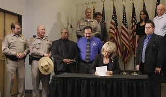 ** FILE ** With law enforcement supporters behind her, Arizona Gov. Jan Brewer signs immigration bill SB1070 into law on Friday, April 23, 2010, in Phoenix. The sweeping measure, major portions of which a federal court later blocked from implementation, would require local law enforcement to question people about their immigration status if there is reason to suspect they are in the country illegally. (AP Photo/Ross D. Franklin)