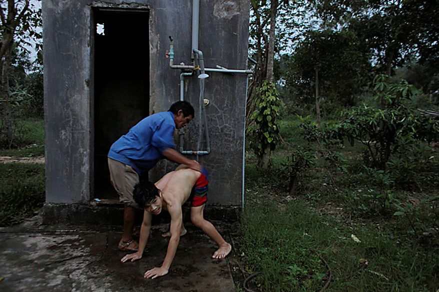 In this photo taken on Oct. 4, 2009, Tran Van Tram, 60, gives his son Tran Van Lam, a bath in the yard next to their home in the village of Cam Tuyen, Vietnam. Tran Van Lam was born with profound physical and mental disabilities that his family, and local officials say, were caused by his parents&#x27; exposure to the chemical dioxin in the defoliant Agent Orange. (AP Photo/David Guttenfelder)