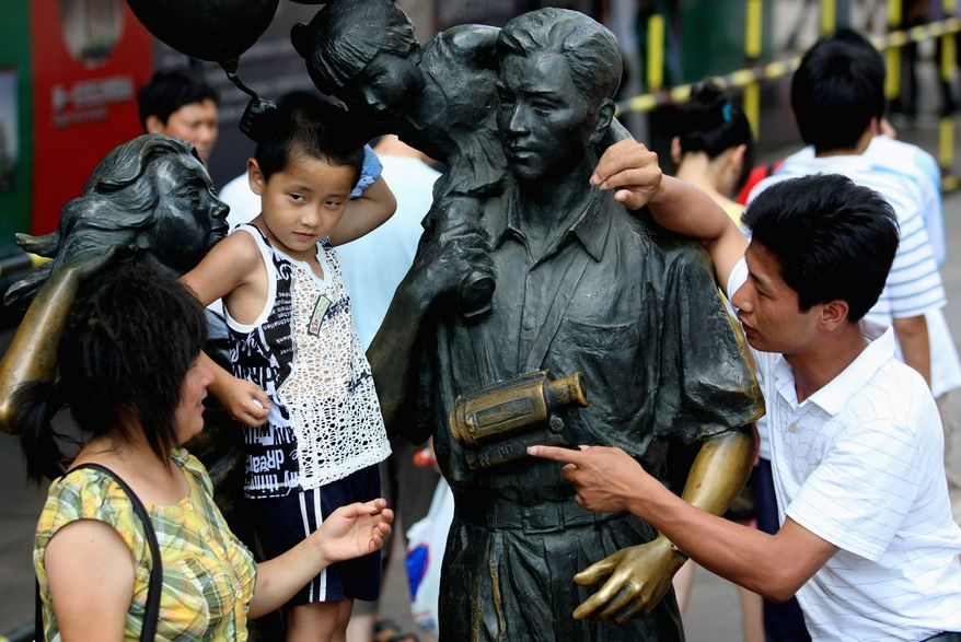 **FILE** A family stands next to a statue depicting a typical Chinese family with one child in Shanghai in 2008. (Associated Press)