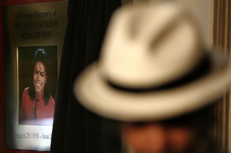 Ricko Baird, a performer from the 'Thriller Live' show poses in the foreground, in front of the commemorative plaque to mark the anniversary of the death of U.S. performer Michael Jackson, as it is unveiled at the Lyric Theatre in London's West End, Thursday, June 24, 2010. After his death on June 25, 2009, the Lyric Theatre has become a focus for fans who created a shrine of flowers, candles, and tributes as it is the home to the 'Thriller Live' show celebrating the music of Jackson and the Jackson 5. (AP Photo/Akira Suemori)