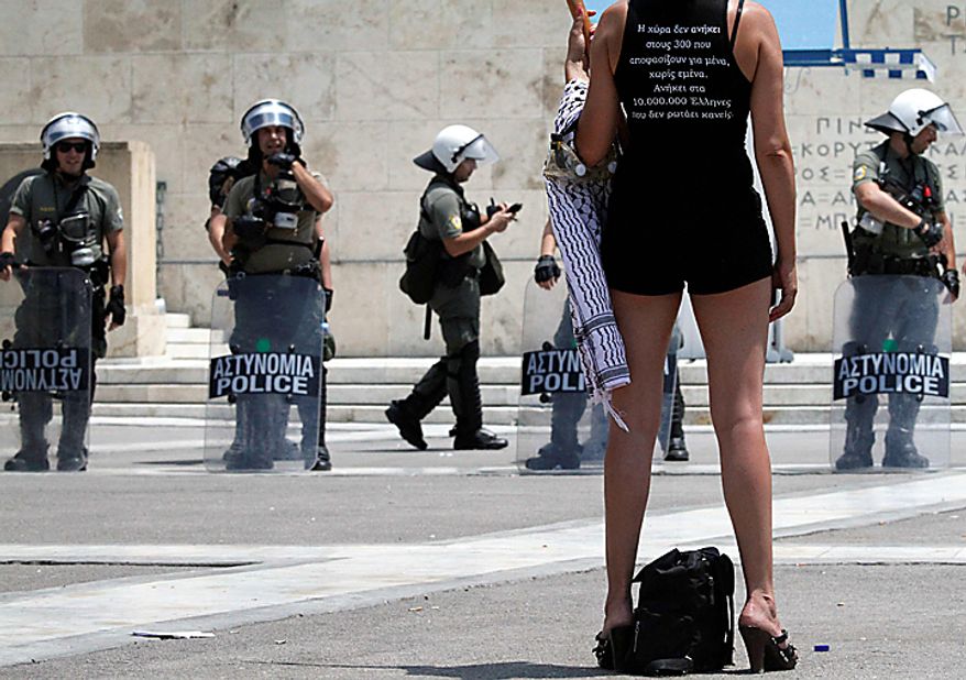 A protester stands in front of riot police outside parliament during a rally in central Athens, Thursday, July 8, 2010. More than 12,000 people took part in two separate protest marches, according to police estimates. Greece's governing Socialists are battling growing discontent as a new round of economic austerity faces party dissent, growing public hostility and fresh strike. The slogan on the T-shirt reads: "This country does not belong to the 300 (members of parliament) but the 10 million Greeks." (AP Photo/Dimitri Messinis)
