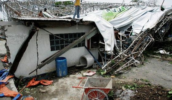 Philippines workers try to arrange a tarpaulin Wednesday from a billboard that collapsed on top of a house south of Manila due to strong winds from Typhoon Conson. (Associated Press)