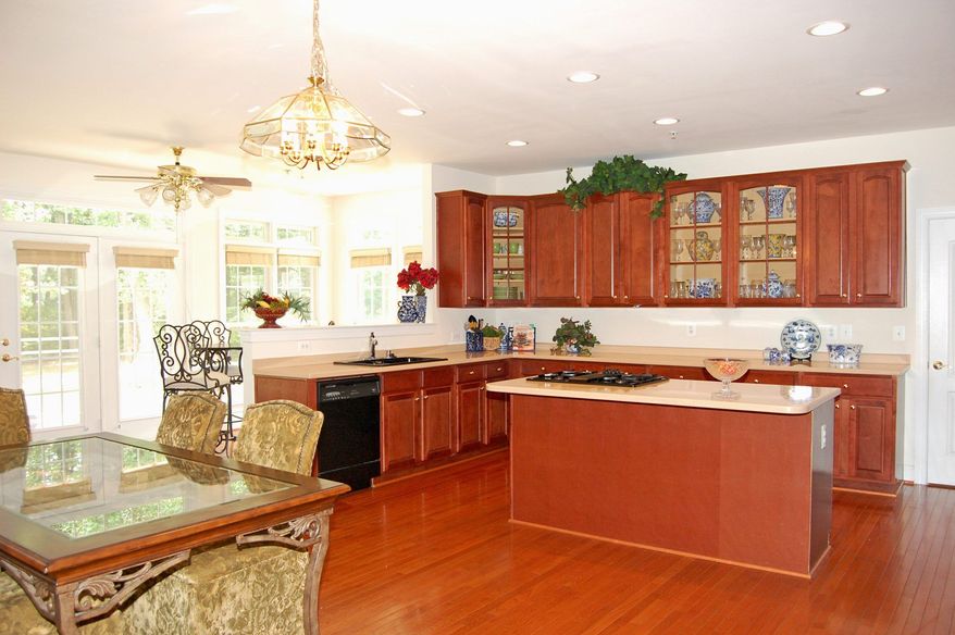 The kitchen has an L-shaped counter and a center island that serves as a breakfast bar and also has a cooktop. The cabinetry coordinates with the hardwood floors. The owners opted to add a bump-out that extends the kitchen and adds a breakfast room.
