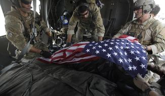In this photograph made on Thursday July 29, 2010, upon landing after a helicopter rescue mission, Tech. Sgt. Jeff Hedglin, right, an Air Force Pararescueman, or PJ, drapes an American flag over the remains of the first of two U.S. soldiers killed minutes earlier in an IED attack, assisted by fellow PJs, Senior Airman Robert Dieguez, center, and 1st Lt. Matthew Carlisle, in Kandahar province, southern Afghanistan. July 2010 was the deadliest month for American forces in the nearly 9-year Afghan War. (AP Photo/Brennan Linsley)