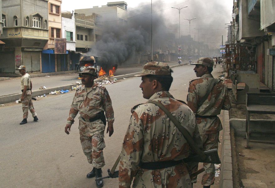 Pakistani para military troops gather near a vehicle set on fire by angry mob following the killing of a local leader of the Muttahida Quami Movement in Pakistan on Tuesday, Aug. 3, 2010. Gunmen killed dozens of people in Pakistan's largest city after the assassination of a lawmaker, officials said Tuesday. (AP Photo/Shakil Adil)