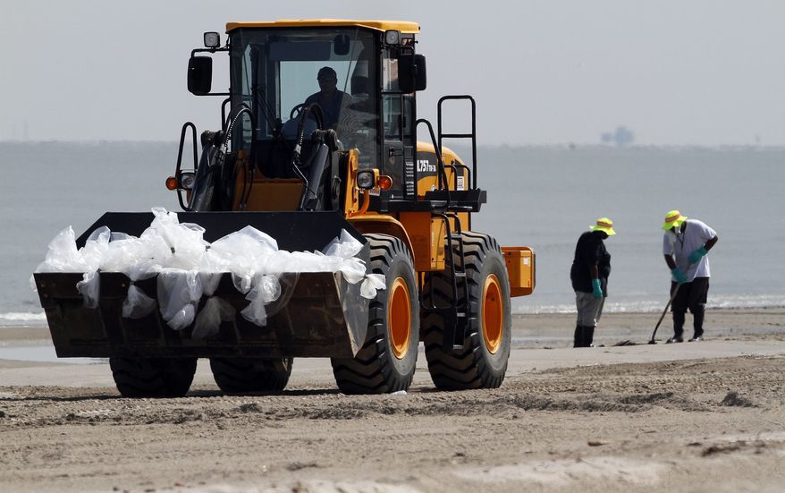 In this Aug. 5, 2010, photo, a bulldozer hauling oiled sand drives past workers as they search for signs of oil on a beach in Grand Isle, La. (AP Photo/Patrick Semansky)