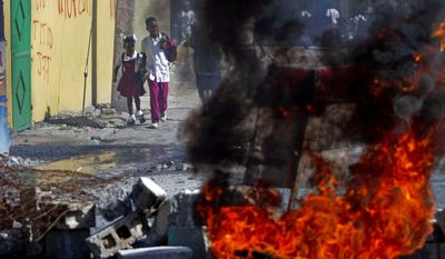 Students walk by burning debris set afire in protest of the Haitian government's lack of help to rebuild the area after the earthquake in Port-au-Prince. Education is one of the areas Haitian candidate for president Wyclef Jean hopes to improve. (Associated Press)