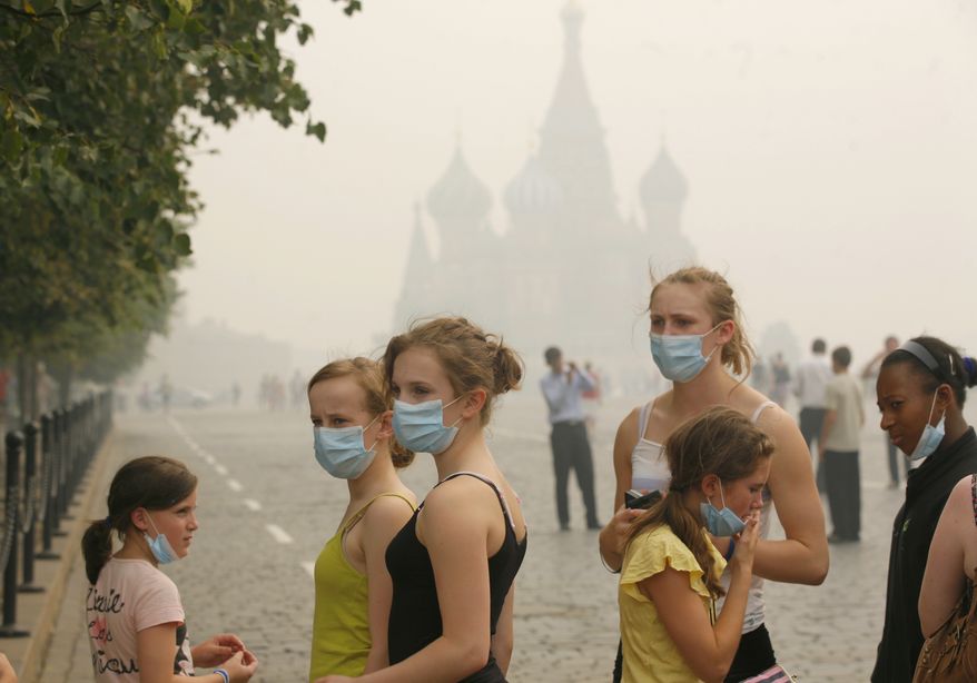 Unidentified American tourists brave the thick blanket of smog covering Moscow as they visit Red Square, with St. Basil's Cathedral in the background, on Sunday, Aug. 8, 2010. (AP Photo/Pavel Golovkin)