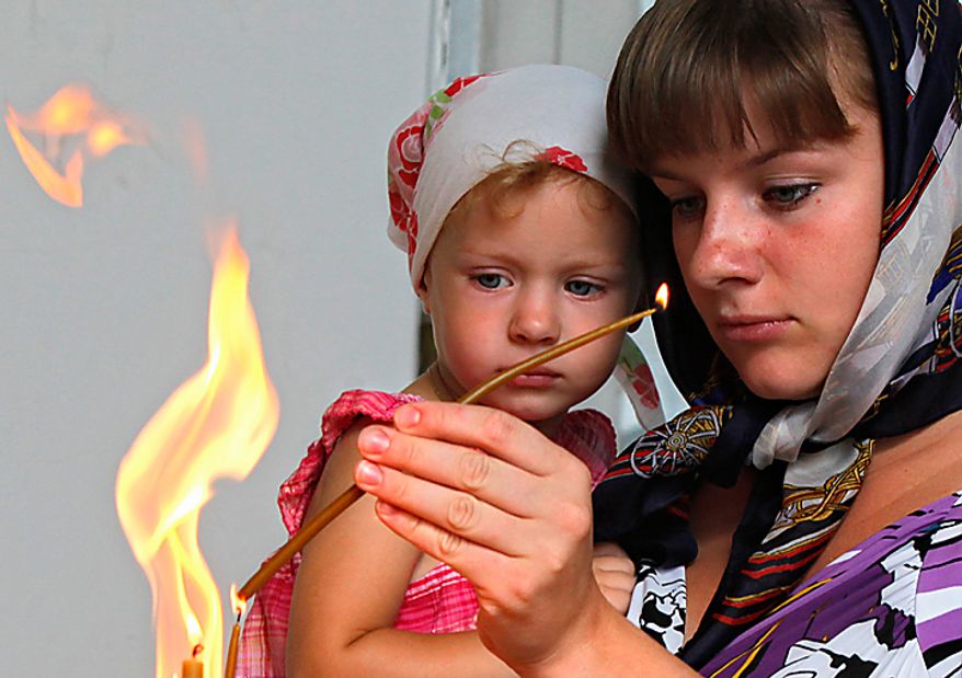 A woman, no name given, prepares to place a candle tribute at the St. Nicolas Cathedral in St.Petersburg, where the lists of seamen who perished in submarine disasters are displayed, Thursday, Aug. 12, 2010. Russian navy ships are flying flags at half-mast and memorial ceremonies are being held across the nation to commemorate the 10th anniversary of the Kursk nuclear submarine disaster. (AP Photo/Dmitry Lovetsky)
