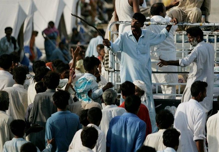 A man uses a stick to ward off survivors as relief goods are distributed Wednesday at a camp in Punjab province. Desperately needed international donations have picked up, but at the same time, militants have taken advantage of the chaos to go on attack. (Associated Press)