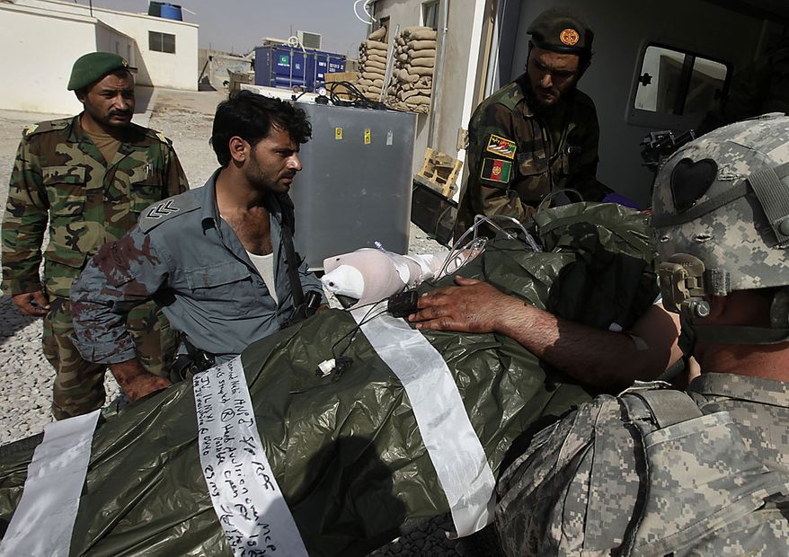 An Afghan National Police officer covered in the blood of his wounded comrade watches as he is loaded into an ambulance by U.S. Army medics and Afghan soldiers for transport to a helicopter landing zone, during an ongoing firefight outside the wire of the Afghan and U.S. Forward Operating Base Howz-e-Madad, operated by the 2nd Battalion, 502nd Infantry Regiment of the 101st Airborne Division, in Zhari district, Kandahar province, southern Afghanistan, Friday, Aug. 20, 2010. The 101st Airborne's 2-502 and their Afghan Army partners operate in a district which, as the birthplace of the Taliban movement, continues to hold many well-armed fighters, and a support network which provides the fighters with improvised explosives and safe havens. (AP Photo/Brennan Linsley)