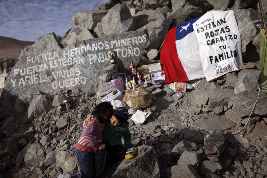 Elias Sepulveda (right) embraces her cousin Katherine on Monday, Aug. 23, 2010, in front of a tribute site with candles, flags and messages for their relatives Esteban and Pablo Rojas, two of the 33 miners trapped at the collapsed mine in Copiapo, Chile. The message at top left reads: "Be strong brother miners, be strong Esteban, Pablo, Tono and Ariel. Let's go Queero." At right, the message says, "We love you Esteban Rojas Carrizo, your family." (AP Photo/Roberto Candia)