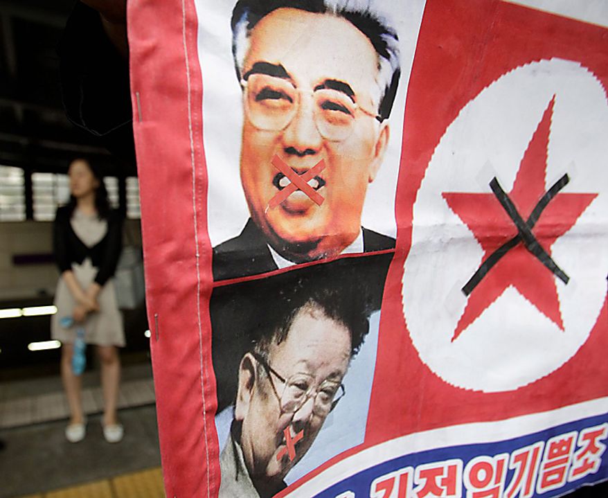 A woman walks by a North Korean flag attached with pictures of North Korean founder late Kim Il Sung, top, and his son, current North leader Kim Jong Il during a rally held against pro-North Korean groups in Seoul, South Korea, Thursday, Sept. 9, 2010. The youngest son of leader Kim Jong Il is widely expected to make his public debut as the Dear Leader's heir apparent at a rare Workers' Party convention, the nation's biggest political gathering in 30 years. (AP Photo/ Lee Jin-man)