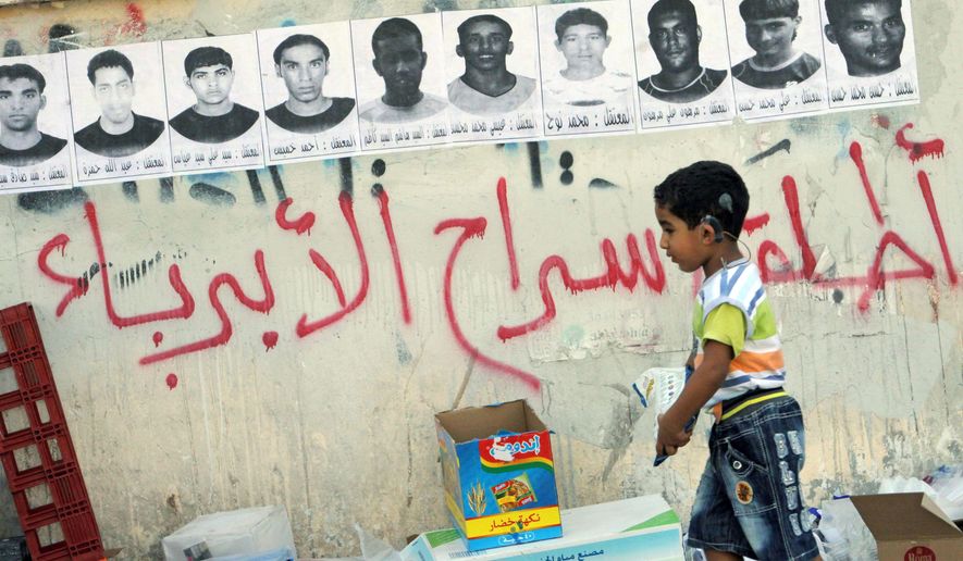 &#x27;FREE THE INNOCENT PEOPLE&#x27;: A child passes by posters of detainees hanging on a wall in a village in Malkiya, Bahrain. Graffiti calls for their release. (Associated Press)