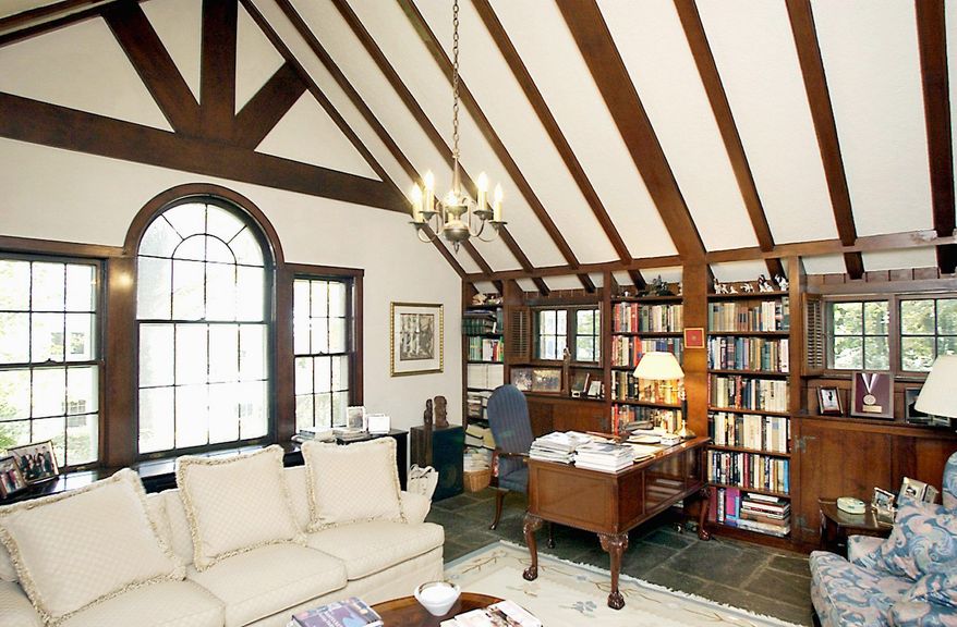 The library has a wood-beamed cathedral ceiling and a Palladian window that overlooks the garden. Built-in mahogany shelves, cabinets and paneling line the room.