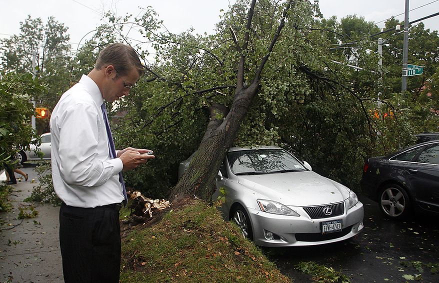 Chris Acheson, of Floral Park, N.Y., checks his cell phone after a severe storm knocked a tree over and onto his car in the Queens Borough of New York, Thursday, Sept. 16, 2010. (AP Photo/Daniel P. Derella)