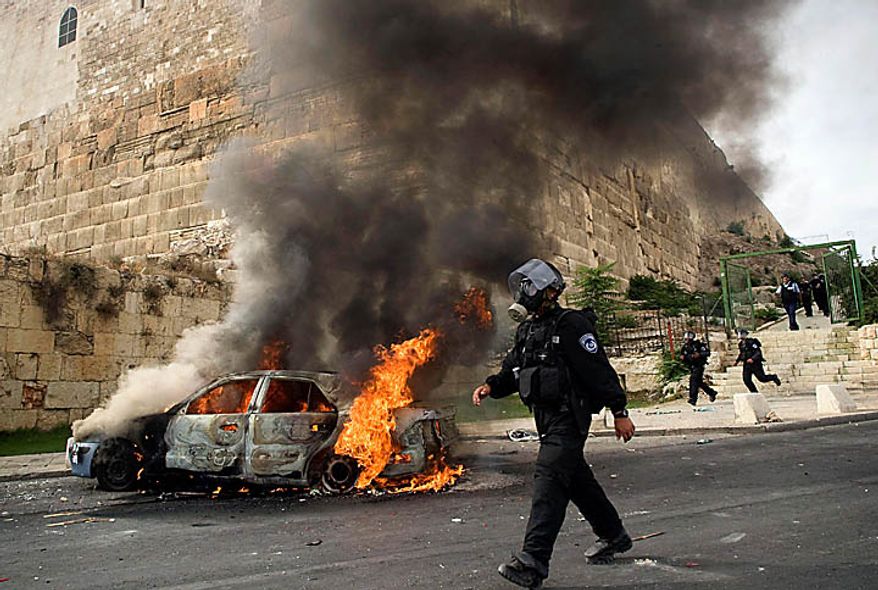 An Israeli police officer wearing a gas mask walks past a car set on fire by Palestinian rioters during clashes outside Jerusalem's Old City, Wednesday, Sept. 22, 2010. Violence erupted after a 32-year-old Palestinian laborer was killed by a private security guard watching over Jewish families in the Silwan neighborhood in east Jerusalem. During the man's funeral, a mob of protesters set tires on fire, smashed the windows of several buses and called for revenge. (AP Photo/Sebastian Scheiner)