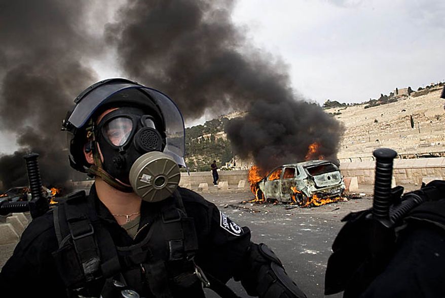 An Israeli police officer wearing a gas mask walks past a car set on fire by Palestinian rioters during clashes outside Jerusalem's Old City, Wednesday, Sept. 22, 2010. Violence erupted after a 32-year-old Palestinian laborer was killed by a private security guard watching over Jewish families in the Silwan neighborhood in east Jerusalem. During the man's funeral, a mob of protesters set tires on fire, smashed the windows of several buses and called for revenge. (AP Photo/Sebastian Scheiner)