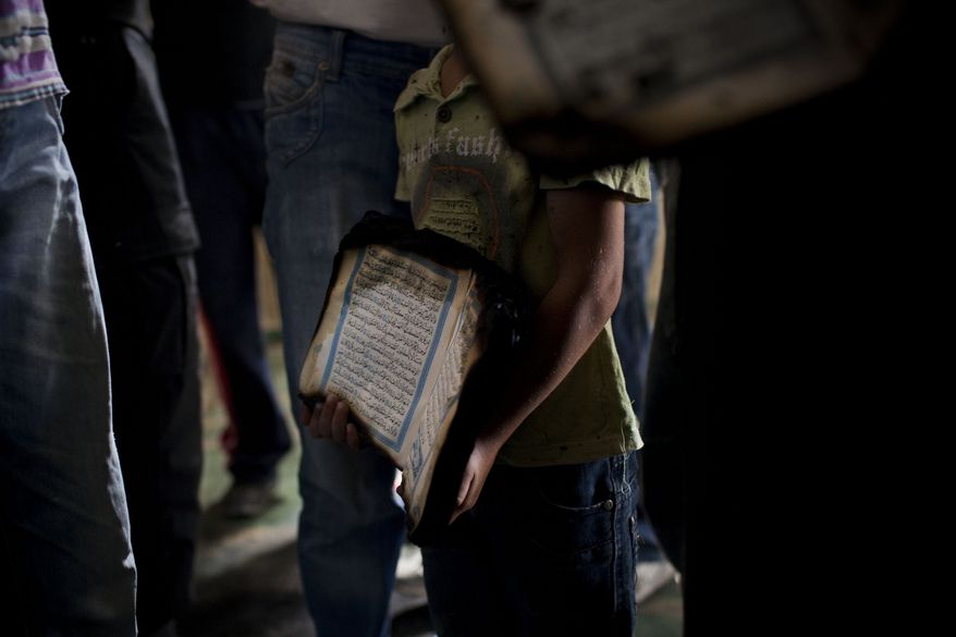 A Palestinian child holds a charred Koran inside a mosque in the West Bank village of Beit Fajjar, near Bethlehem, on Monday, Oct. 4, 2010, after arsonists, scrawling "Revenge" on a wall in Hebrew, torched the mosque. The blaze threatens to stoke new tensions over deadlocked Mideast peacemaking. (AP Photo/Bernat Armangue)