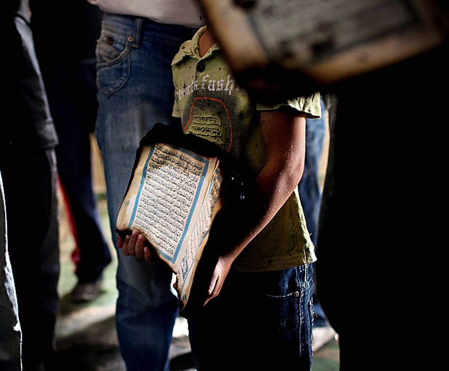 A Palestinian child holds a charred Quran, a Muslim holy book, inside a mosque in the West Bank village of Beit Fajjar, near Bethlehem, Monday Oct. 4, 2010. Arsonists torched a mosque in a Palestinian village in the West Bank on Monday, scrawling "revenge" on a wall in Hebrew and charring copies of the Muslim holy book in a blaze that threatened to stoke new tensions over deadlocked Mideast peacemaking. (AP Photo/Bernat Armangue)