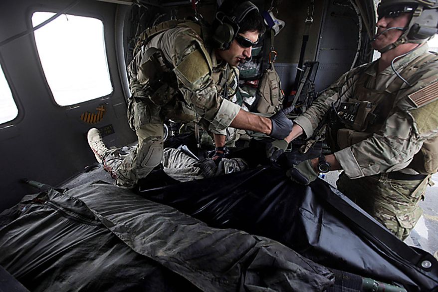 In this Thursday July 29, 2010 file picture, Tech. Sgt. Jeff Hedglin, right, and Senior Airman Robert Dieguez, both U.S. Air Force Pararescuemen, or PJs, place into a body bag, the remains of one of two U.S. soldiers killed minutes earlier in an IED attack, as soldiers, unseen wait to carry them away, upon landing after a helicopter rescue mission in Kandahar province, southern Afghanistan. (AP Photo/Brennan Linsley, File)