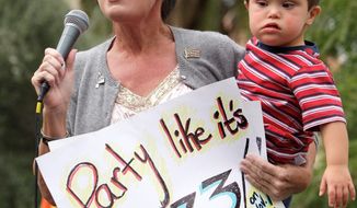 ** FILE ** In this Oct. 26, 2010, file photo, former Alaska Gov. Sarah Palin holds son Trig as she addresses a Tea Party Express rally at the Arizona Capitol in Phoenix. The sign is a reference to the Boston Tea Party. (Associated Press)