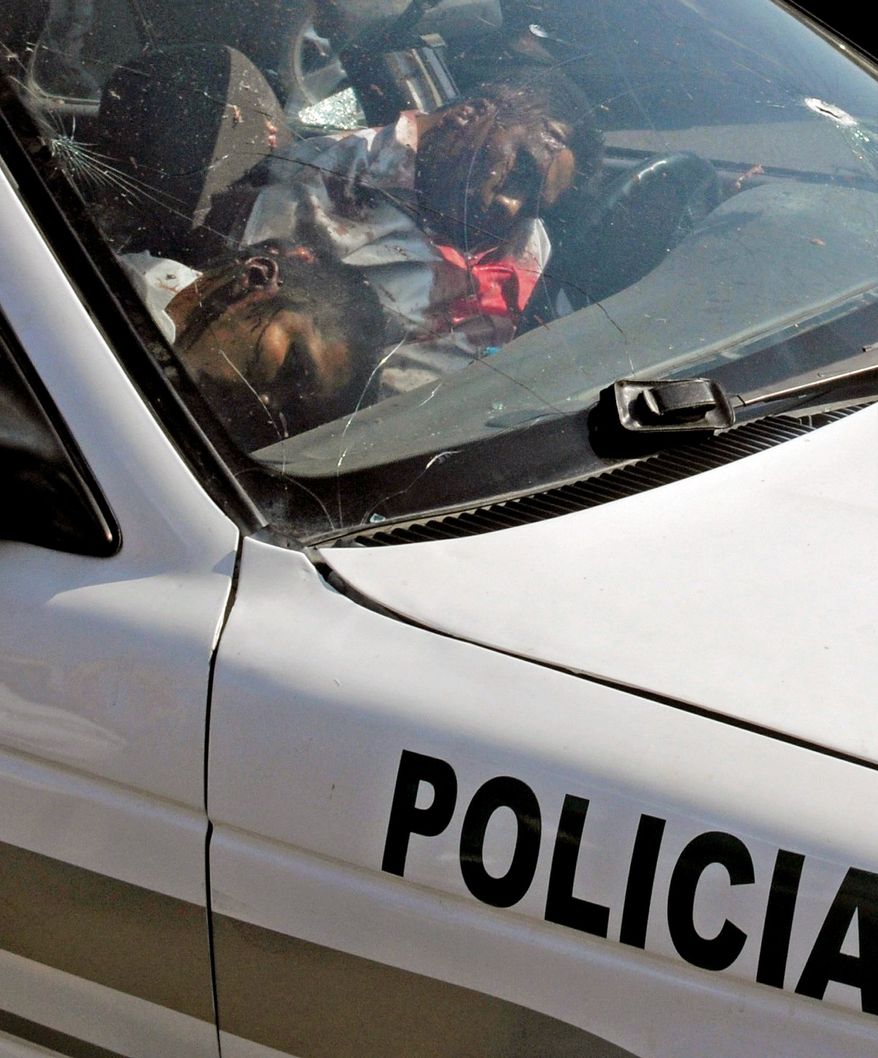 The bodies of two dead traffic police officers remain in their patrol car in Acapulco on Thursday. Gunmen killed four police officers the day after a grave holding at least 18 bodies was found. (Associated Press)
