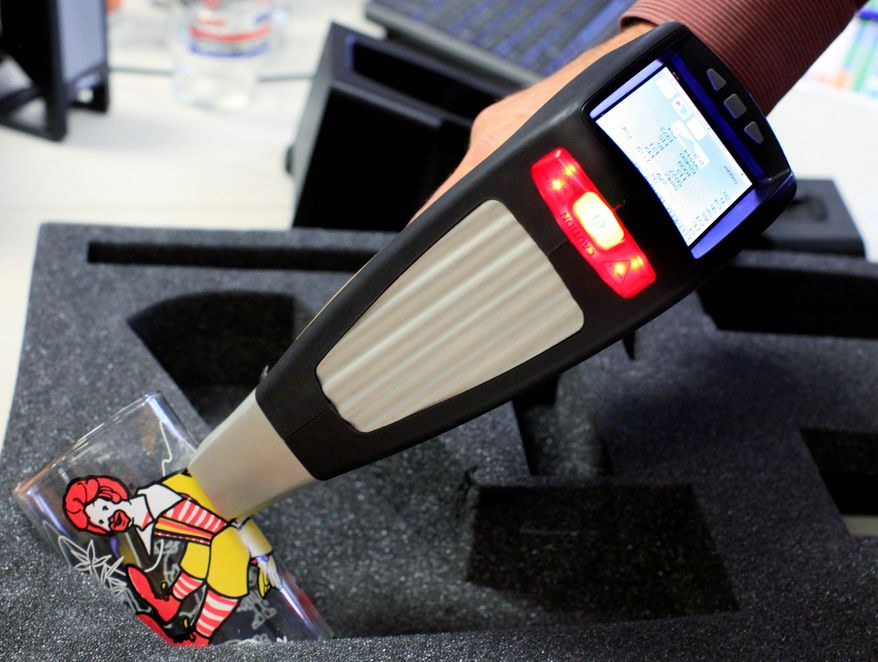 A hand-held device tests a Ronald McDonald glass for cadmium, lead and other toxic elements. Federal regulators have said such glasses are subject to standards for children's products. (Associated Press)